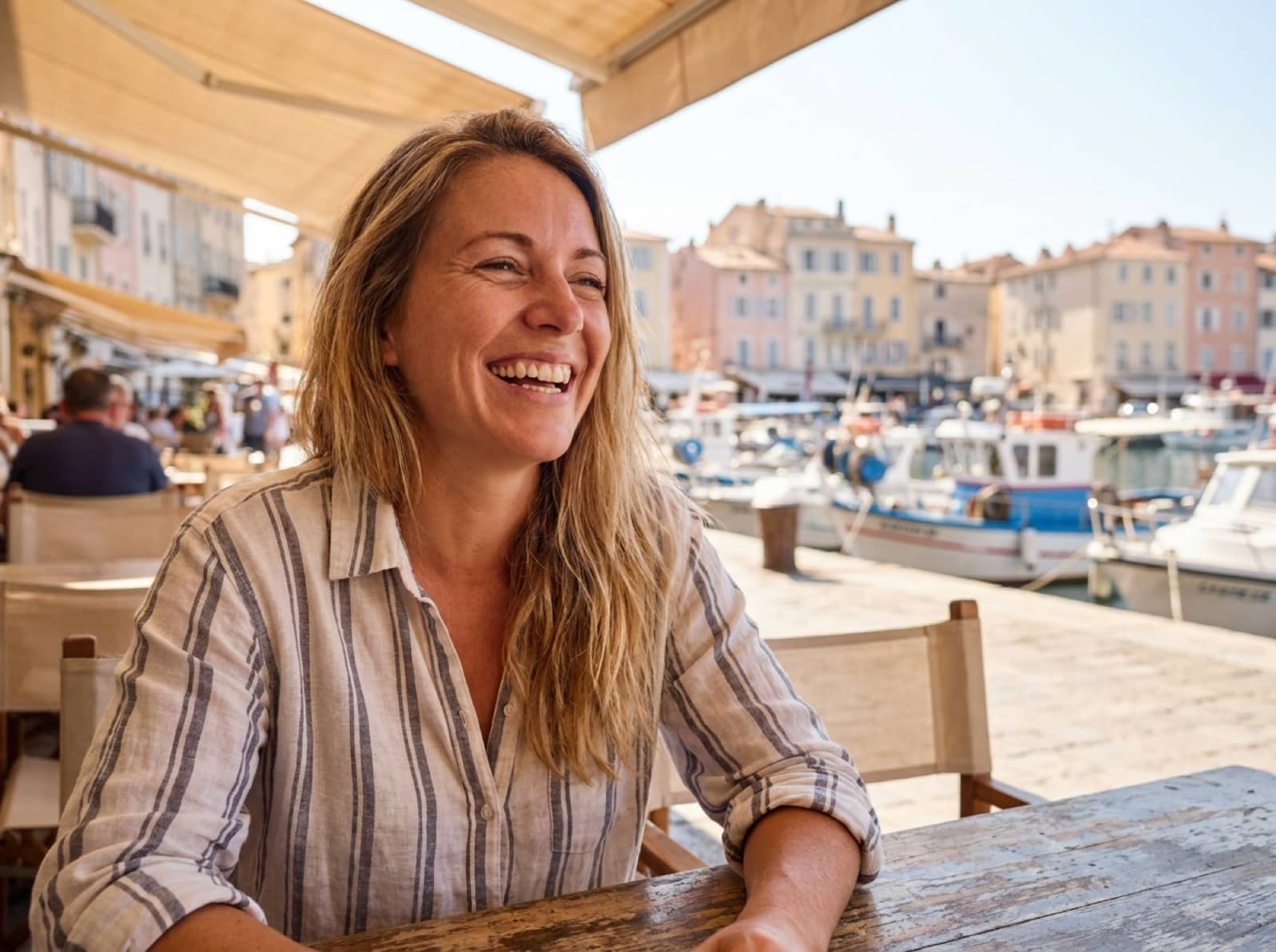 Frau lacht entspannt in einem Hafencafé während eines Sommerurlaubs